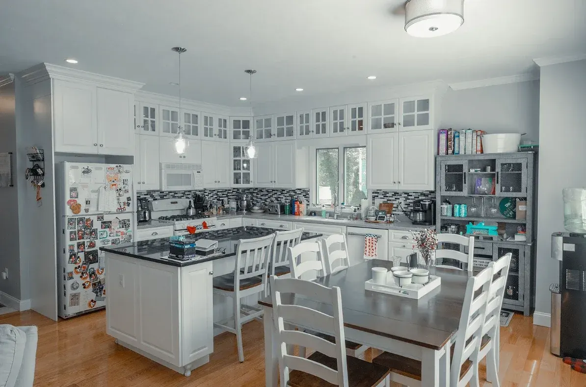 Cocina luminosa con gabinetes blancos, isla y mesa de comedor